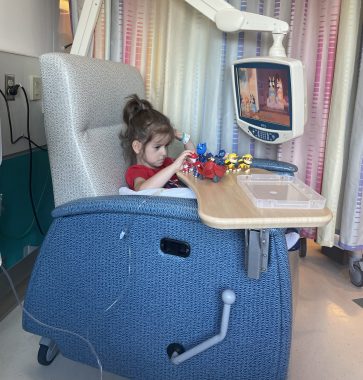 Nexviazyme | Pompe Disease News | Cayden sits in a big, blue infusion treatment chair at the clinic. He plays with toys on a table, and a video screen hovers above.