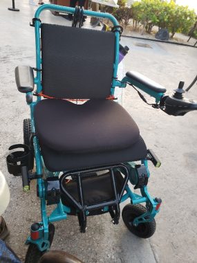 An electric Fold&Go wheelchair with blue-green trim and black seat cushions sits in a parking lot.