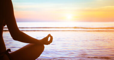 person sitting in yoga pose on beach in front of water