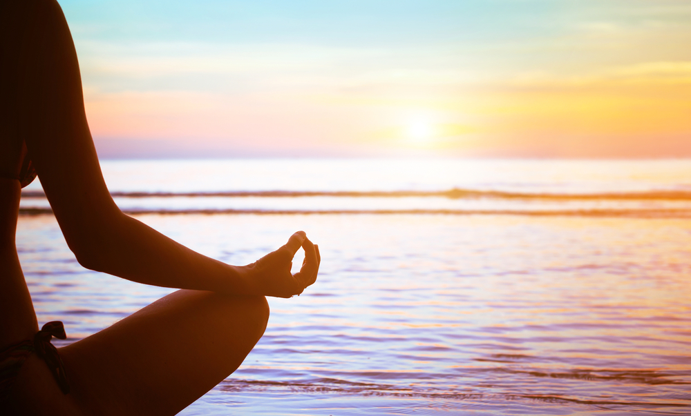 person sitting in yoga pose on beach in front of water