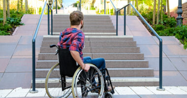 man in wheelchair at the bottom of a set of stairs outside