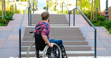 man in wheelchair at the bottom of a set of stairs outside