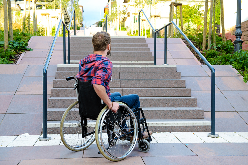 man in wheelchair at the bottom of a set of stairs outside