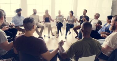 People in a circle sitting in chairs and holding hands in solidarity.