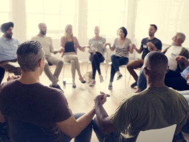 People in a circle sitting in chairs and holding hands in solidarity.