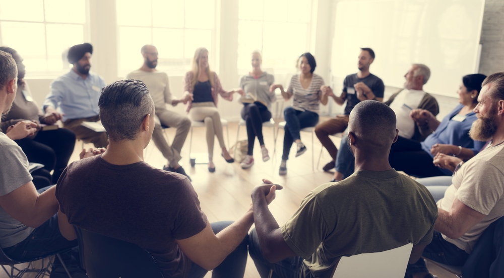 People in a circle sitting in chairs and holding hands in solidarity.