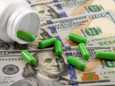 a bottle of pills spilling out on top of $100 bills