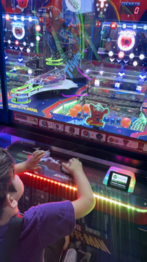 A young boy is deeply engaged in playing a video game. He's got both hands on the controls, but you can't distinguish many other specific details. What's notable about this photos are the bright, multicolored lights of the games and environment in general, as it's a video arcade. 