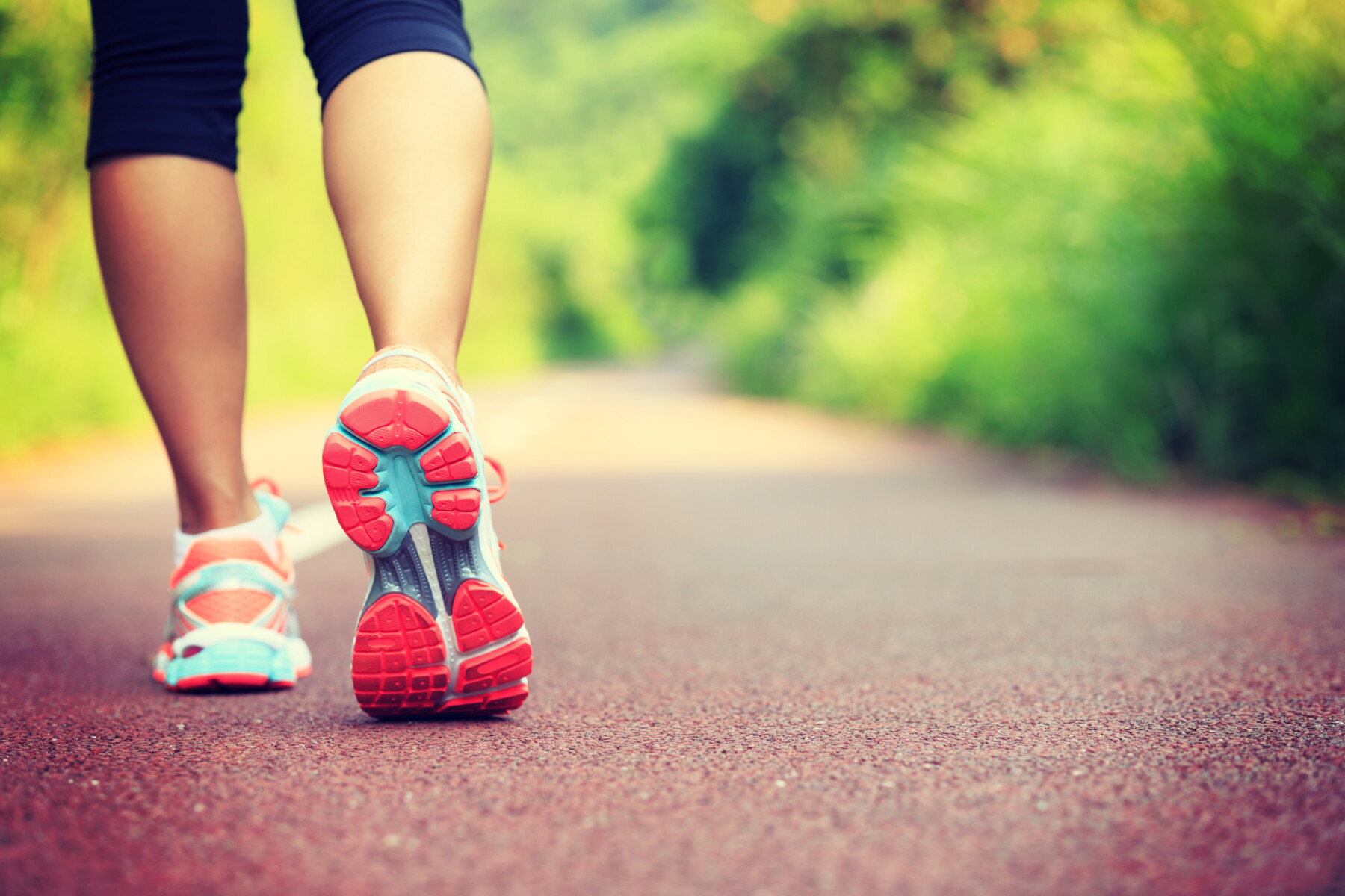 A female walking shown from the calf down on a paved road