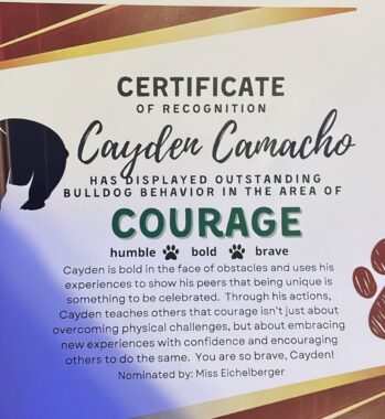 A screenshot of a certificate of recognition made out to Cayden Camacho for "outstanding bulldog behavior in the area of courage." The design includes a bulldog and dog footprints highlighting "humble," "bold," and "brave."